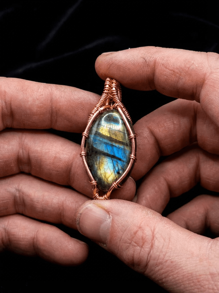 Craftsman's hands holding a handmade copper wire-wrapped labradorite pendant